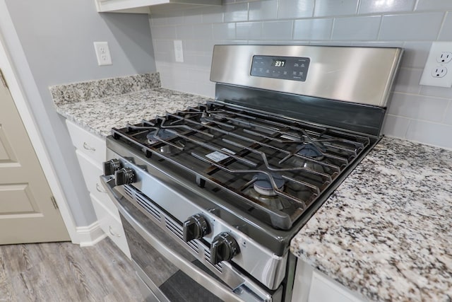 interior details featuring stainless steel range with gas stovetop, light wood-type flooring, light stone counters, decorative backsplash, and white cabinetry