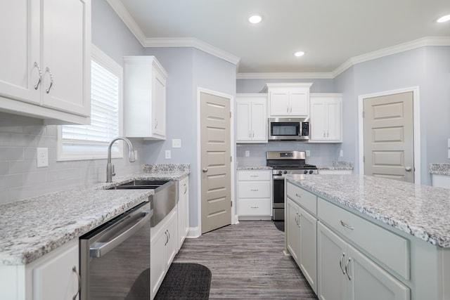 kitchen with ornamental molding, appliances with stainless steel finishes, wood finished floors, white cabinets, and a sink