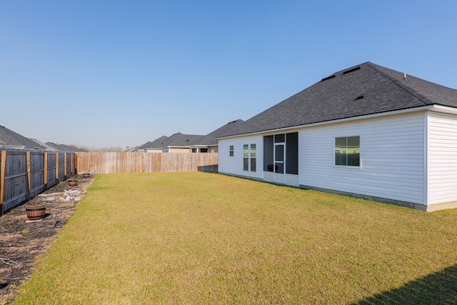 rear view of property with a yard, a shingled roof, and a fenced backyard