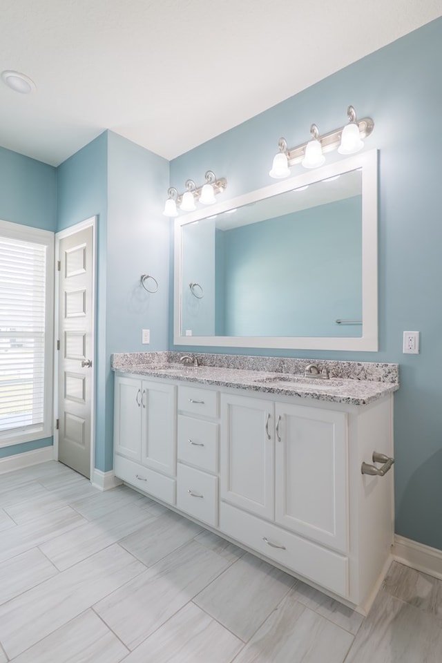 bathroom featuring double vanity, baseboards, and a sink