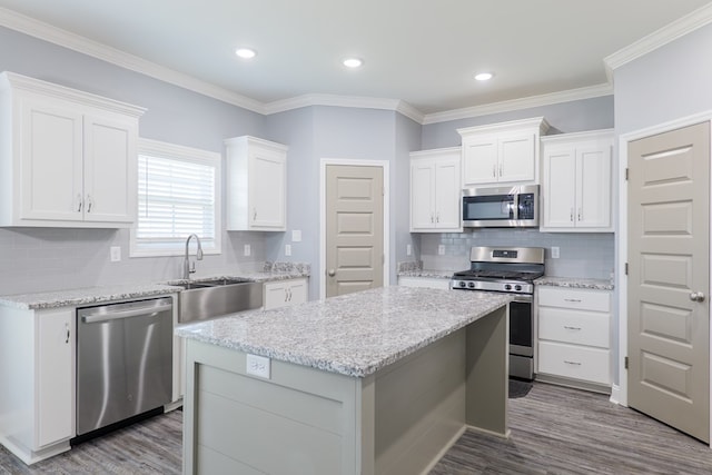 kitchen featuring a kitchen island, wood finished floors, white cabinets, stainless steel appliances, and a sink