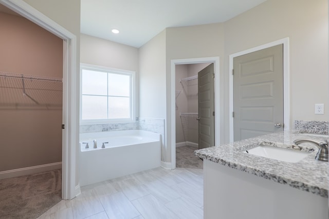 bathroom with a bath, a spacious closet, vanity, and baseboards