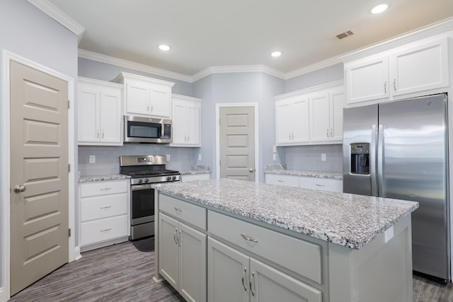 kitchen with visible vents, dark wood-style flooring, ornamental molding, appliances with stainless steel finishes, and a center island