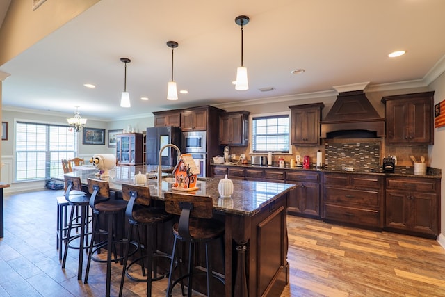 kitchen with premium range hood, hanging light fixtures, a center island with sink, and black appliances