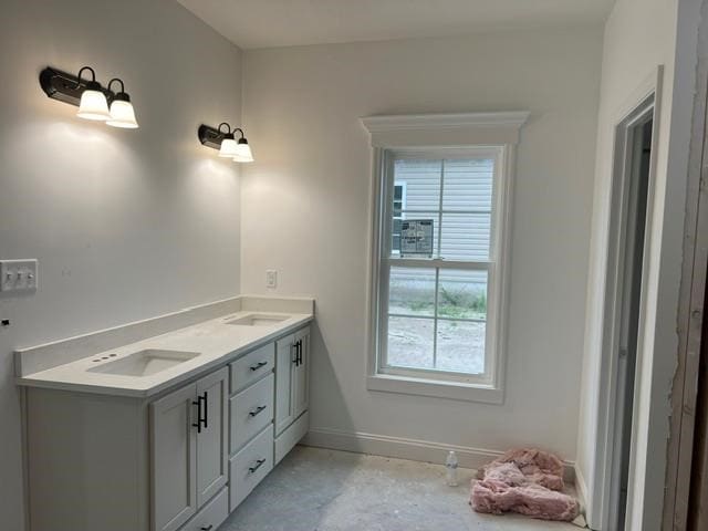 bathroom featuring baseboards, double vanity, a sink, and unfinished concrete floors