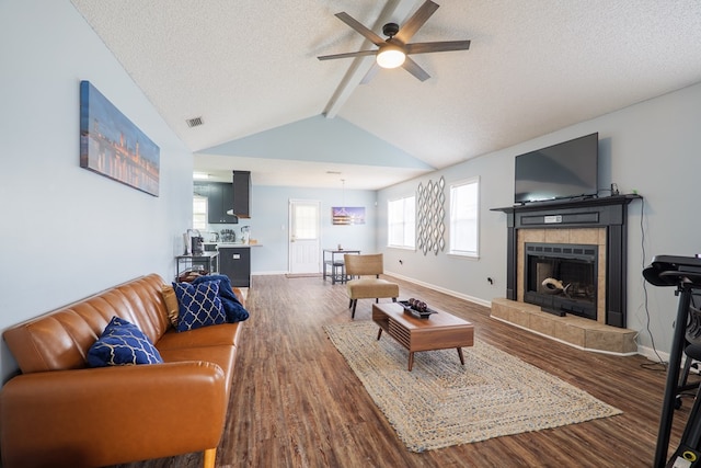 living room with lofted ceiling with beams, dark wood-type flooring, ceiling fan, and a fireplace