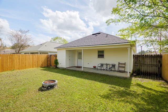 rear view of house featuring a fire pit, a shingled roof, a yard, a fenced backyard, and a patio