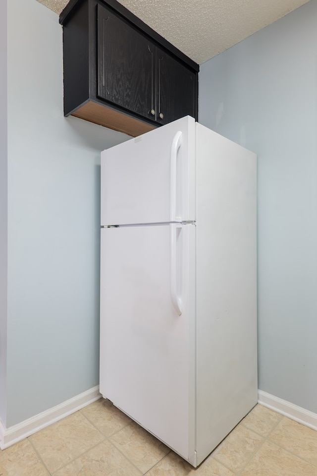 kitchen featuring baseboards, a textured ceiling, dark cabinetry, and freestanding refrigerator