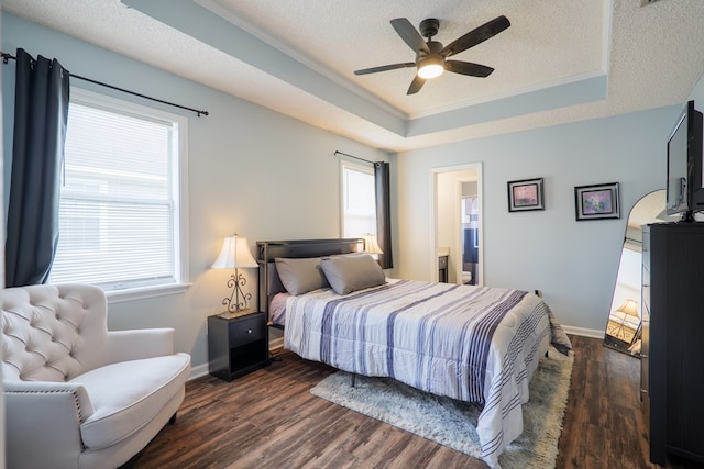 bedroom with baseboards, a tray ceiling, dark wood-style flooring, a textured ceiling, and connected bathroom