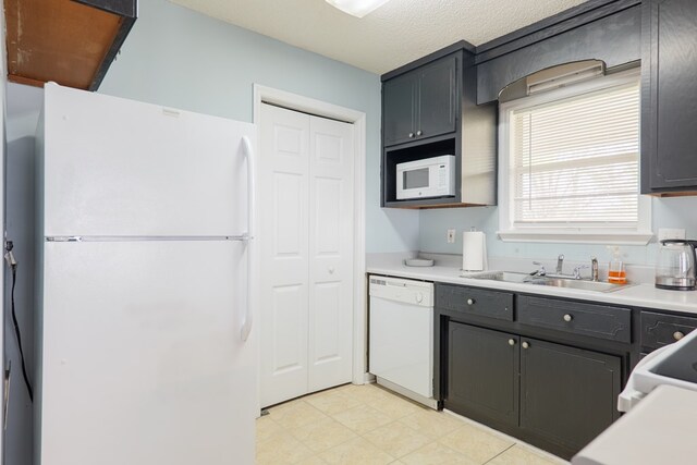 kitchen with white appliances, a textured ceiling, light countertops, and a sink