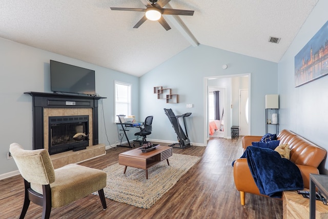 living area featuring visible vents, a ceiling fan, wood finished floors, vaulted ceiling with beams, and a tile fireplace