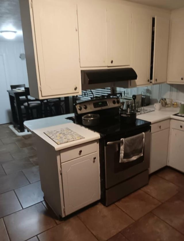 kitchen featuring stainless steel range with electric stovetop, white cabinets, and dark tile patterned floors