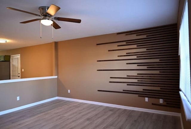 unfurnished room featuring ceiling fan, wood finished floors, and baseboards