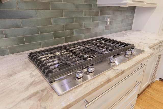 details featuring light stone counters, stainless steel gas stovetop, light hardwood / wood-style floors, and decorative backsplash