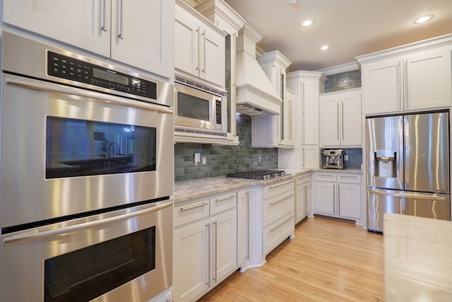 kitchen featuring stainless steel appliances, light stone countertops, custom exhaust hood, and white cabinets