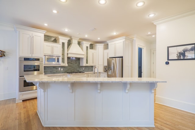 kitchen featuring premium range hood, appliances with stainless steel finishes, white cabinets, a kitchen breakfast bar, and a large island