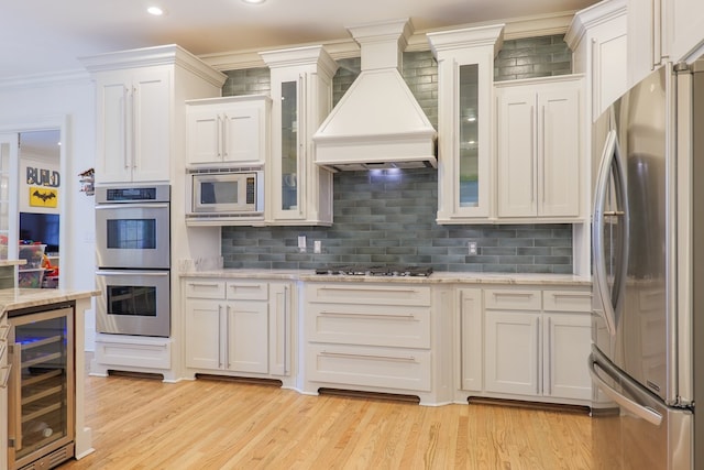 kitchen with premium range hood, appliances with stainless steel finishes, white cabinetry, wine cooler, and crown molding