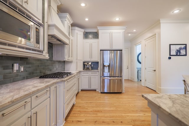 kitchen featuring premium range hood, white cabinetry, ornamental molding, stainless steel appliances, and light stone countertops