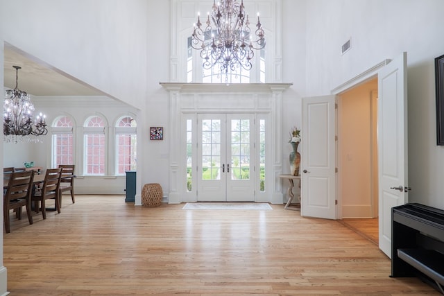 entrance foyer featuring a towering ceiling, an inviting chandelier, ornamental molding, light wood-type flooring, and french doors