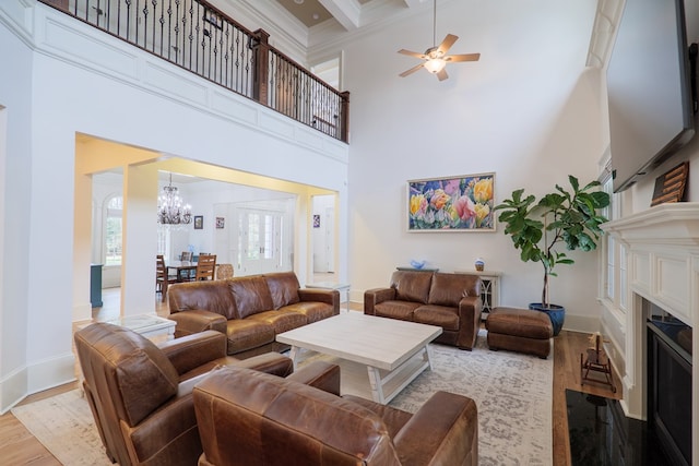 living room featuring a towering ceiling, ceiling fan with notable chandelier, crown molding, beam ceiling, and light hardwood / wood-style flooring