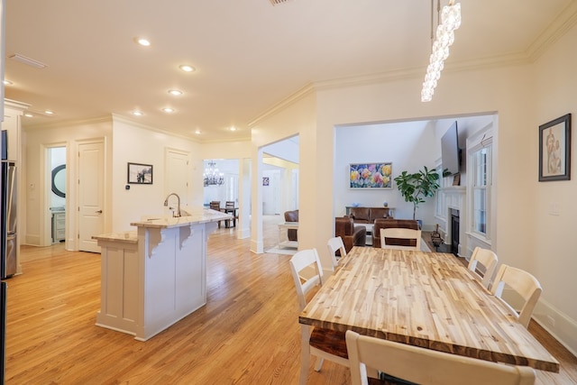 dining room with ornamental molding, sink, a chandelier, and light hardwood / wood-style floors