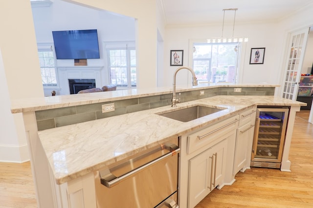 kitchen featuring wine cooler, sink, light stone counters, ornamental molding, and pendant lighting