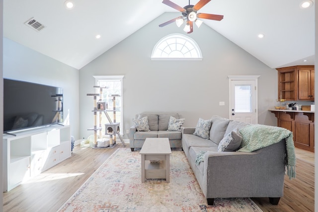 living area with a wealth of natural light, visible vents, light wood-style flooring, and high vaulted ceiling