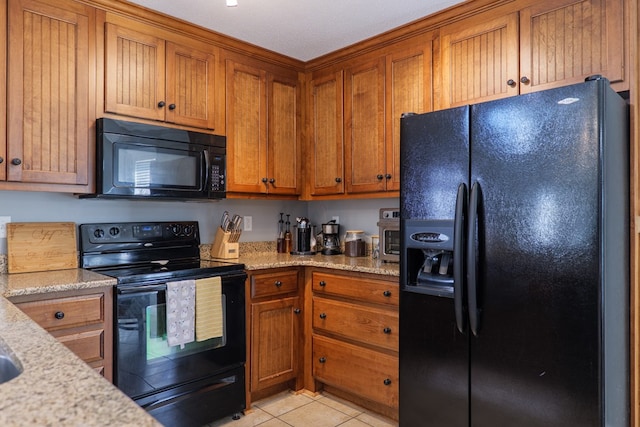 kitchen featuring light tile patterned floors, light stone countertops, black appliances, and brown cabinetry