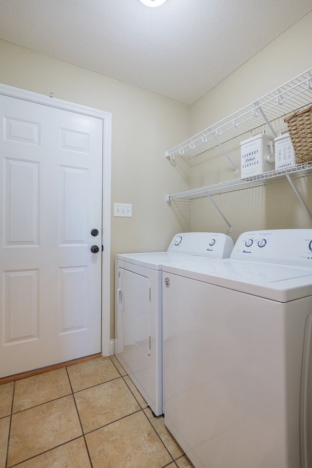 washroom with light tile patterned flooring, laundry area, a textured ceiling, and separate washer and dryer