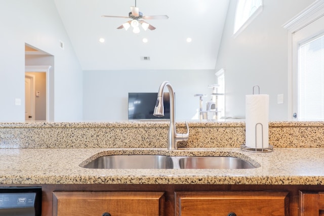 kitchen featuring dishwashing machine, a ceiling fan, light stone countertops, a sink, and vaulted ceiling