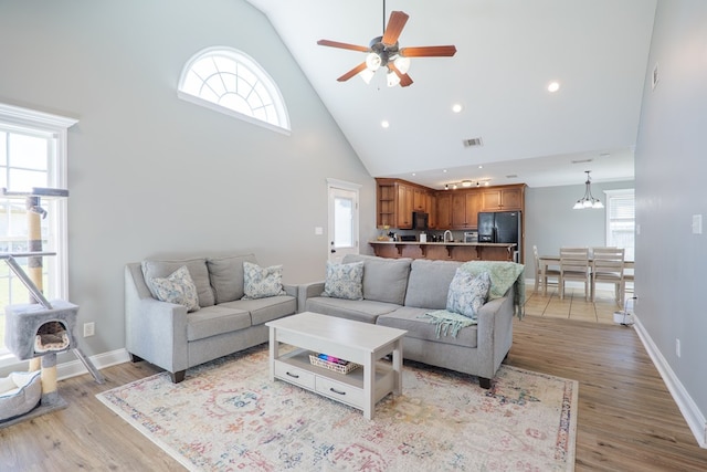 living area with baseboards, visible vents, light wood finished floors, and high vaulted ceiling