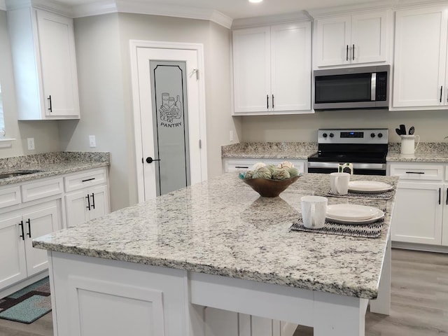 4639 Castle Pines Ln, Lake Park, GA 31636 - kitchen with white cabinets, light wood-style floors, stainless steel appliances, a kitchen island, and ornamental molding