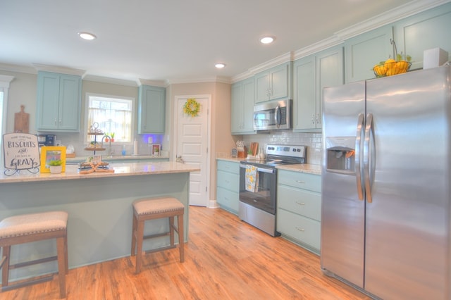 kitchen featuring light wood finished floors, appliances with stainless steel finishes, a breakfast bar area, and ornamental molding