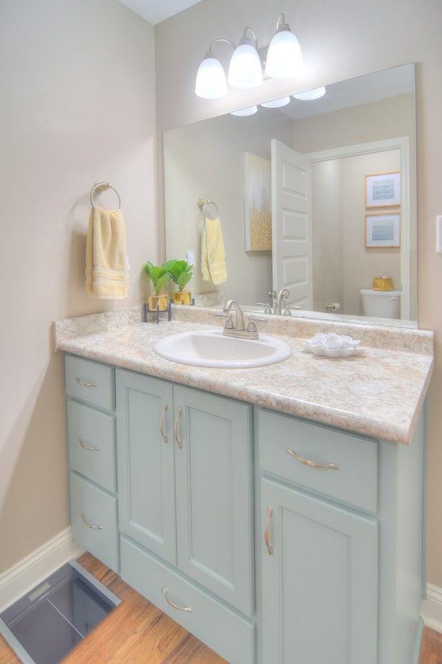 bathroom featuring baseboards, toilet, wood finished floors, and vanity