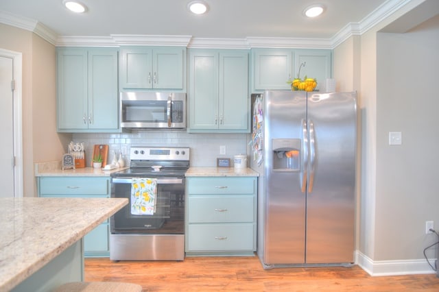 kitchen with blue cabinetry, backsplash, appliances with stainless steel finishes, crown molding, and light wood finished floors