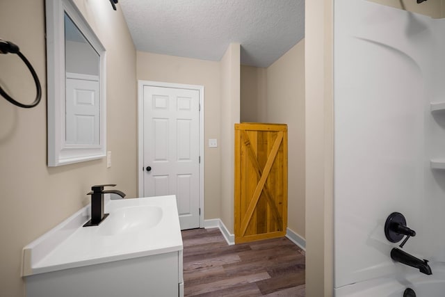 full bath with a textured ceiling, wood finished floors, vanity, baseboards, and  shower combination