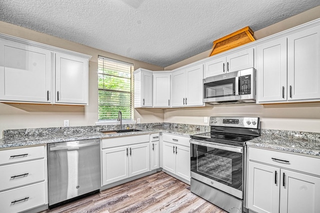 kitchen with stainless steel appliances, light wood-type flooring, a sink, and white cabinets