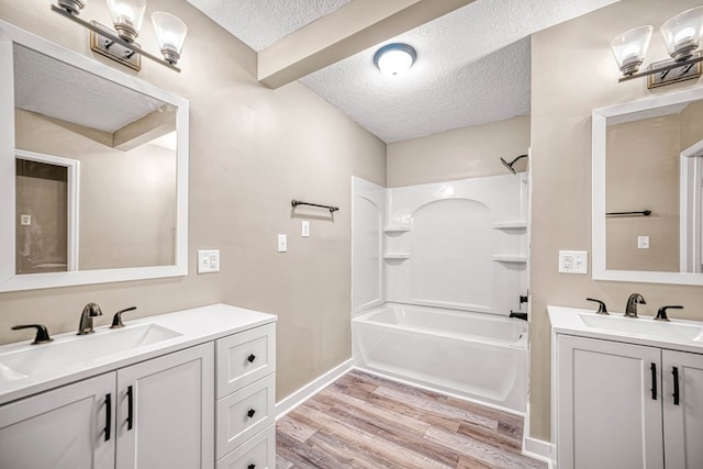 bathroom with a textured ceiling, two vanities, a sink, and wood finished floors