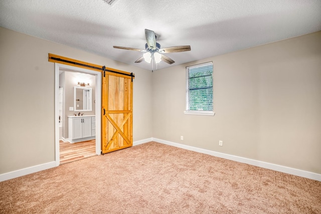 unfurnished room featuring a barn door, a ceiling fan, light carpet, a textured ceiling, and baseboards