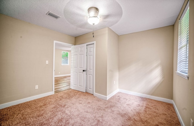 carpeted spare room featuring baseboards, visible vents, and a textured ceiling