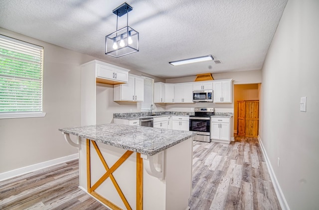 kitchen featuring stainless steel appliances, white cabinets, a sink, light wood-type flooring, and baseboards