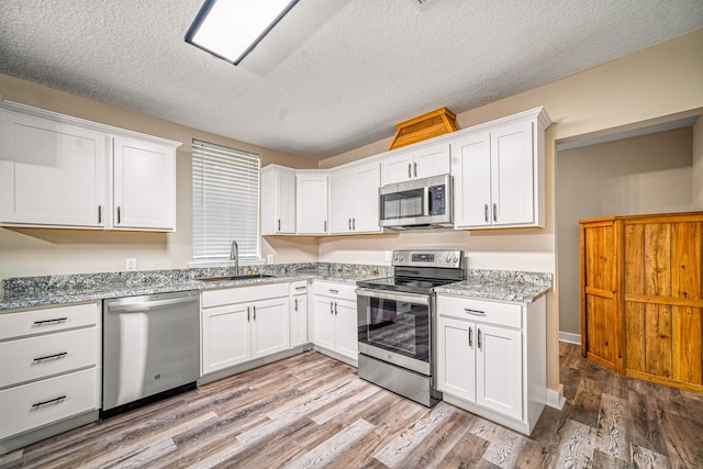 kitchen featuring stainless steel appliances, light wood finished floors, a sink, and white cabinetry