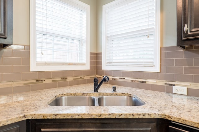 kitchen featuring light stone counters, decorative backsplash, sink, and dark brown cabinets