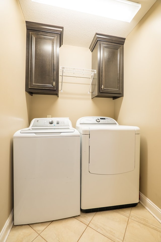 laundry room featuring cabinets, light tile patterned floors, washing machine and clothes dryer, and a textured ceiling