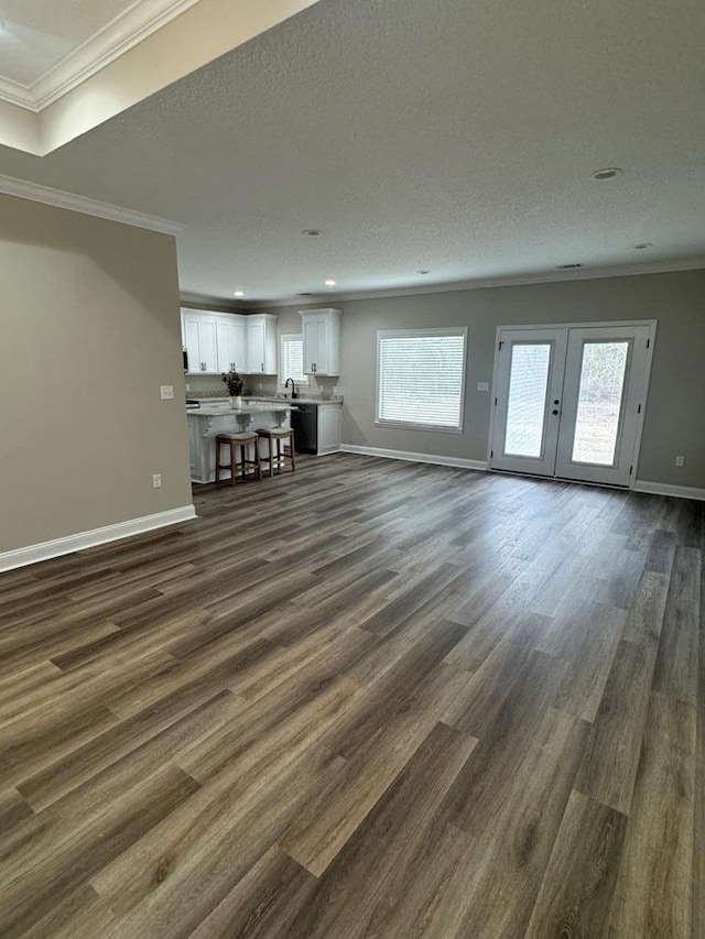 unfurnished living room featuring a textured ceiling, dark wood-type flooring, ornamental molding, and sink