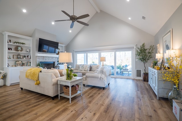 living room with beam ceiling, ceiling fan, a brick fireplace, high vaulted ceiling, and hardwood / wood-style floors