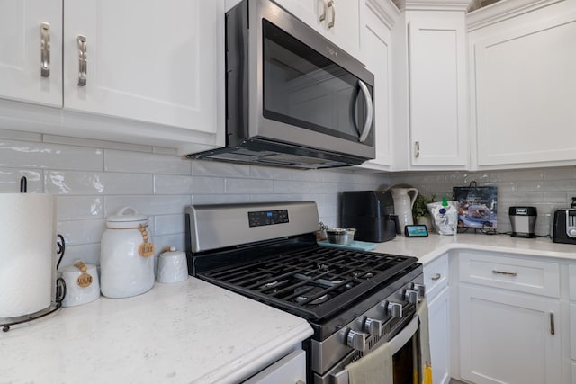 kitchen with white cabinets, appliances with stainless steel finishes, tasteful backsplash, and light stone counters