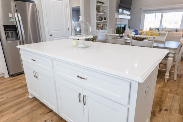 kitchen featuring stainless steel fridge, light wood-type flooring, a fireplace, a kitchen island, and white cabinetry