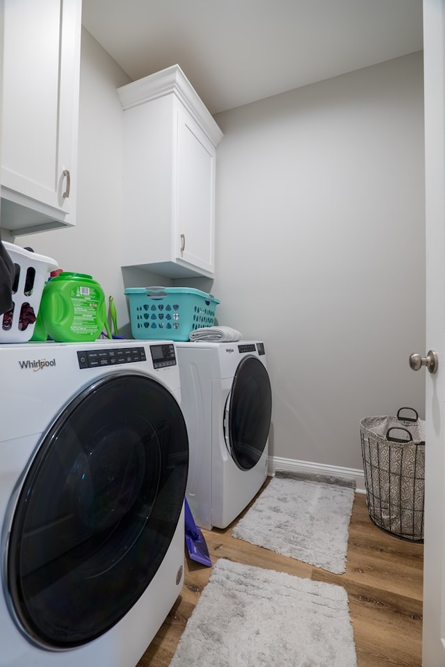 clothes washing area featuring separate washer and dryer, hardwood / wood-style floors, and cabinets