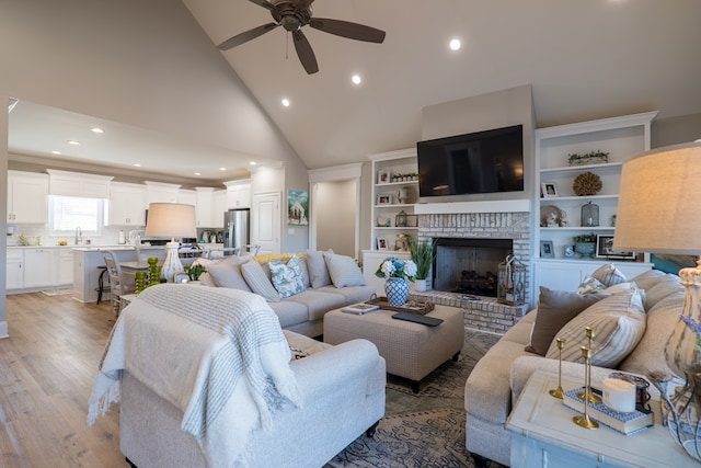 living room featuring ceiling fan, sink, high vaulted ceiling, a fireplace, and light hardwood / wood-style floors